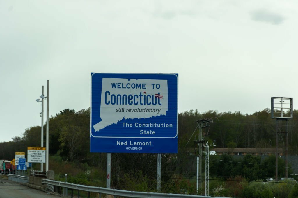 A "Welcome to Connecticut" sign by the roadside with trees in the background.