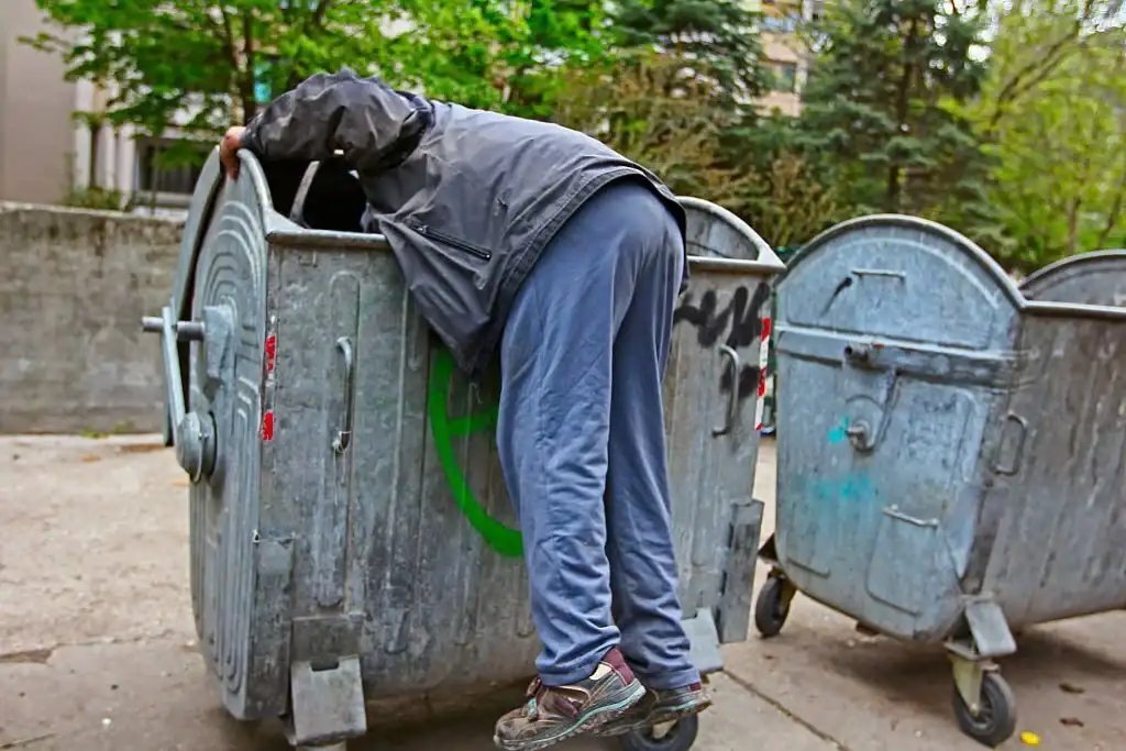 Person leaning into an industrial trash bin on the street.
