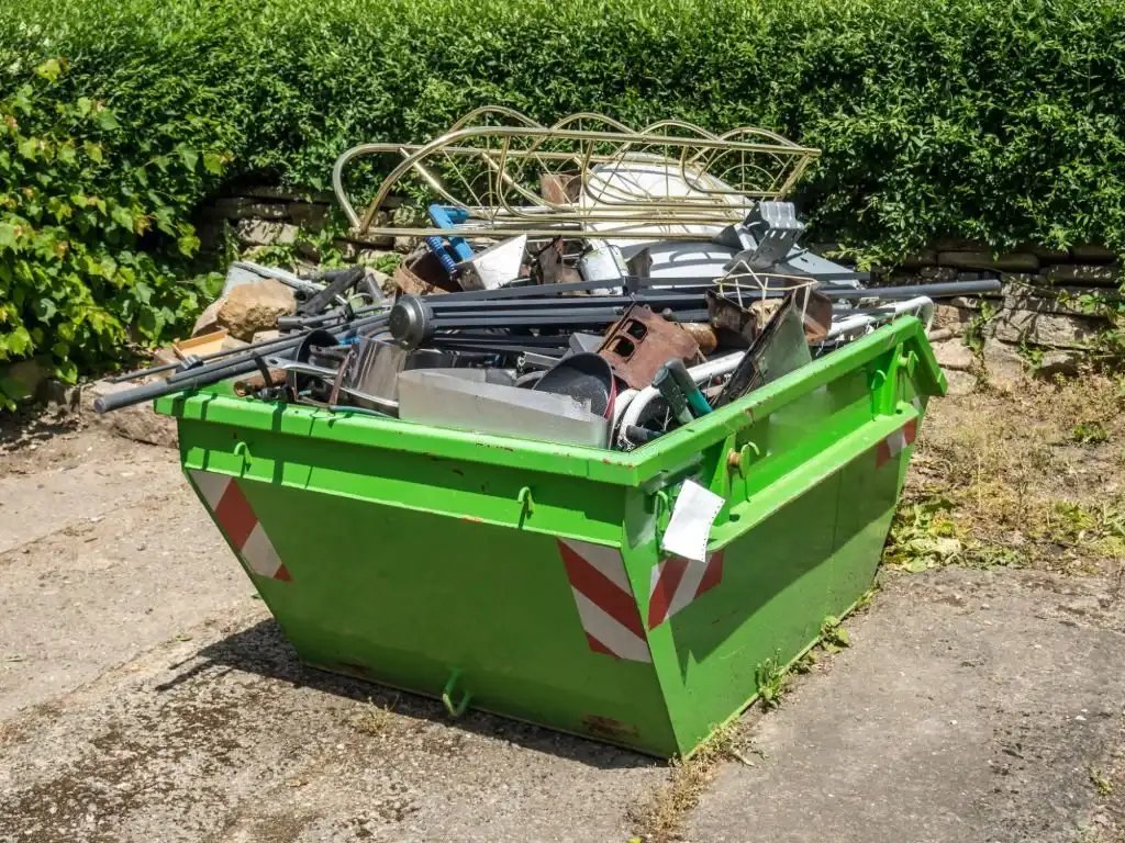 Overflowing green skip bin with assorted waste and scrap metal.