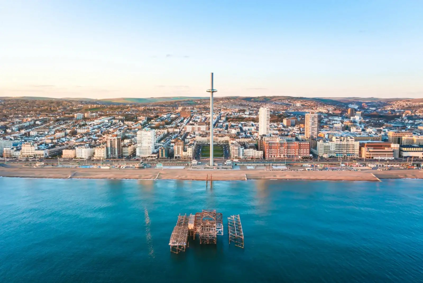 Aerial view of a coastal city with a pier and a tall observation tower during sunset.